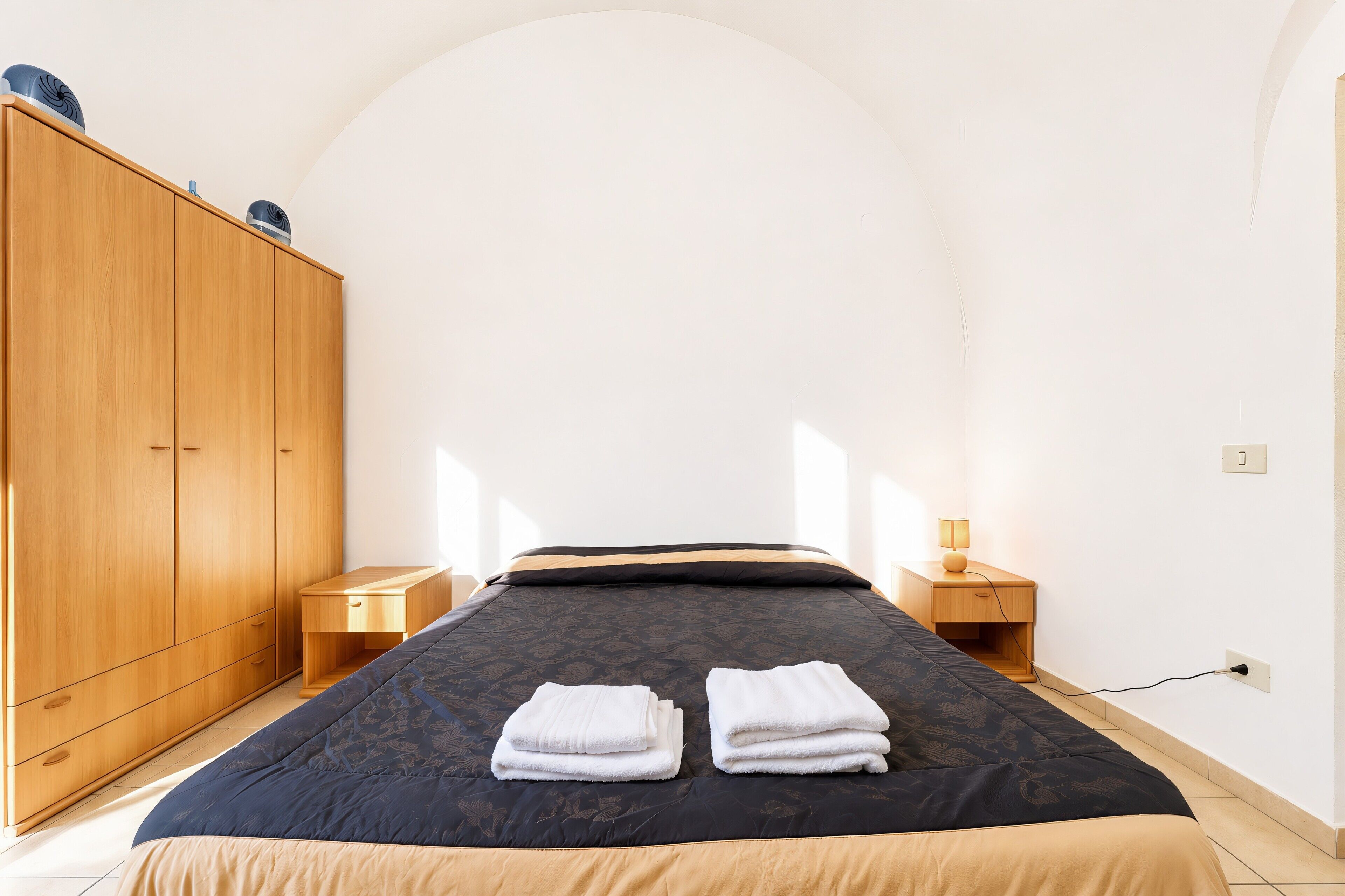 Camera da letto con un letto, un'armadio in legno, comodini e una presa elettrica.