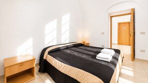 Ein Schlafzimmer mit einem Bett, einem Nachttisch, einer Lampe und einer Tür zu einem anderen Raum.