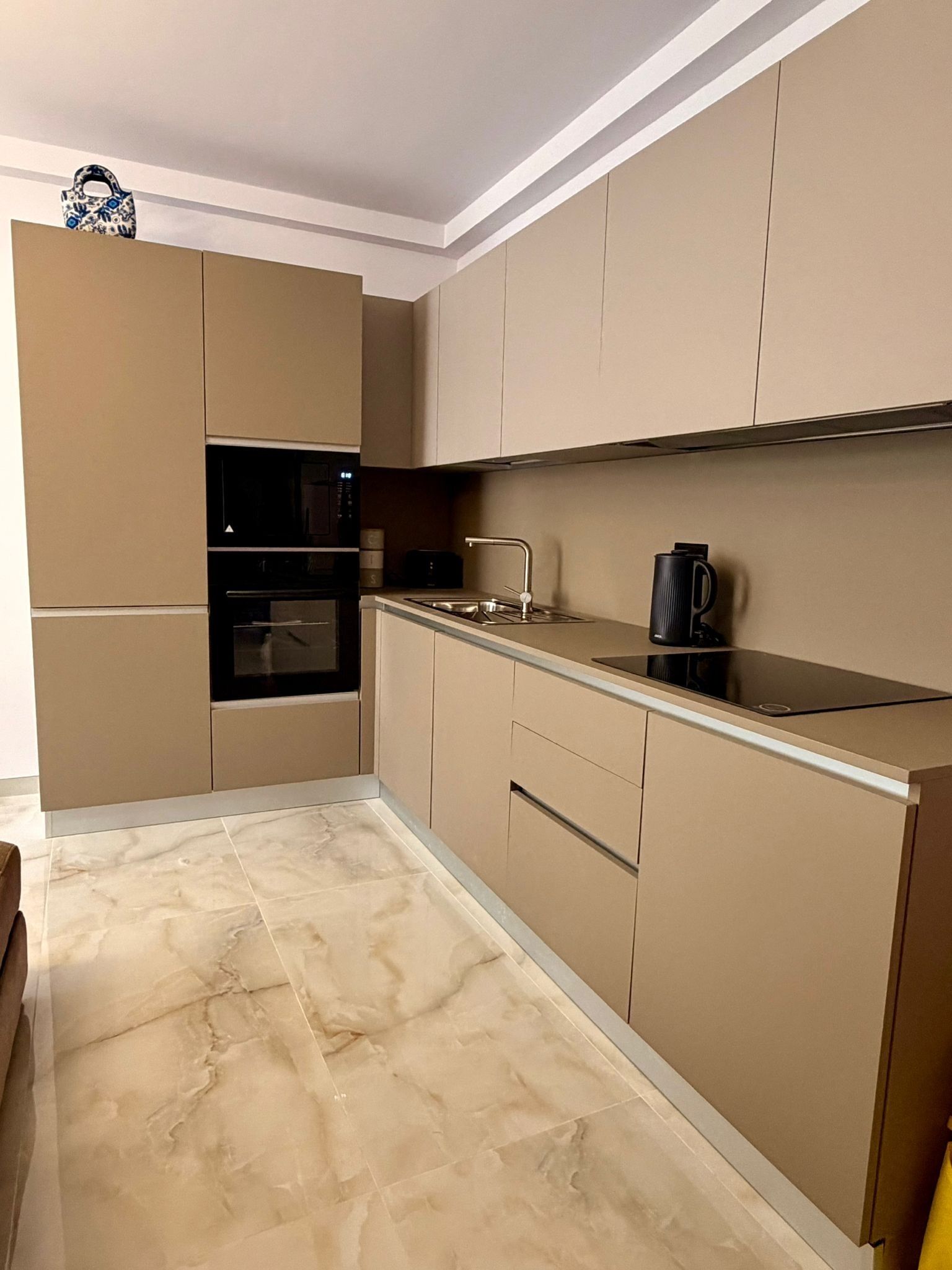 Una cucina moderna con mobili beige, un forno nero, un lavello in acciaio inossidabile e un bollitore nero.