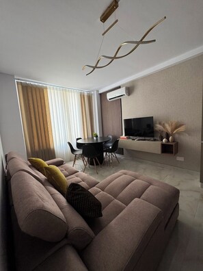 Ein modernes Wohnzimmer mit Sofa, Esstisch und Fernseher.