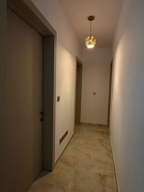 Un couloir avec un luminaire, une porte et un interrupteur mural.