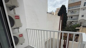Un balcon avec une balustrade blanche, des unités de climatisation et une vue sur les bâtiments voisins.