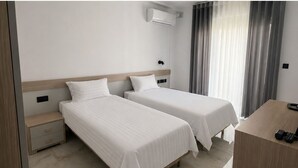 Une chambre d’hôtel avec deux lits, un bureau, une table de chevet, un appareil de climatisation et une fenêtre avec des rideaux.