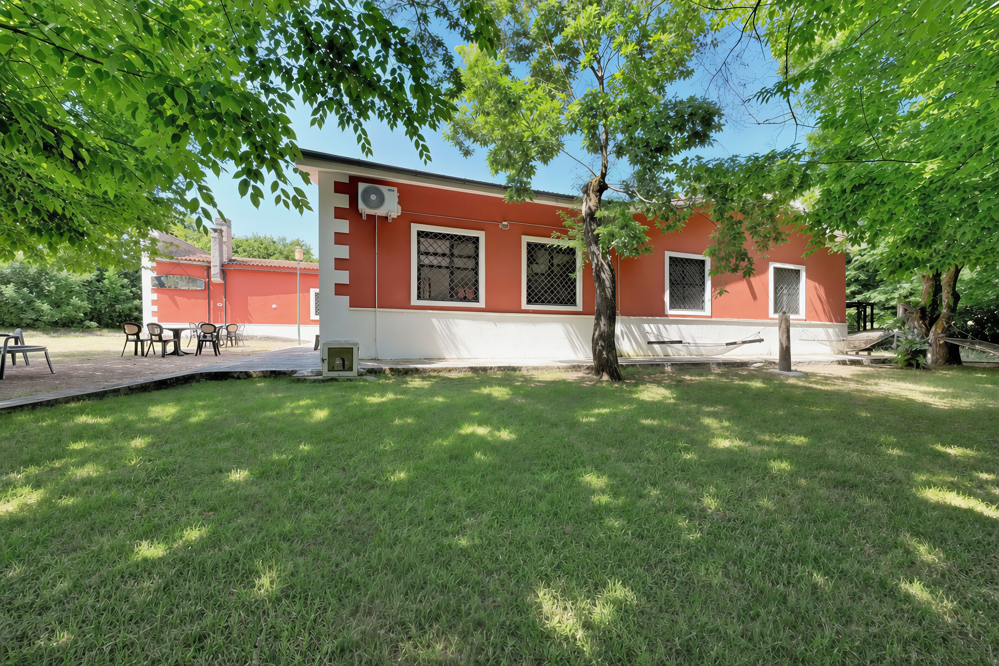 Un bâtiment rouge et blanc doté d’un patio, de places assises extérieures et d’un arbre au premier plan.