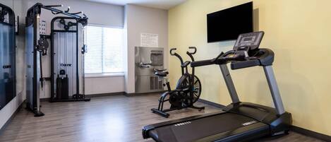 A fitness center with cardio equipment, including a treadmill and an elliptical, and a weight machine.