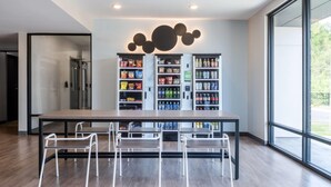 A modern dining area with a long table and four chairs, a snack vending machine, and a large window providing a view of the outdoors.