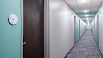 A long, narrow hallway with doors on both sides, a carpeted floor, and a ceiling with recessed lighting.