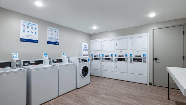 A laundry facility with multiple washing machines, dryers, and control panels. - Echo Suites Extended Stay By Wyndham Savannah Pooler (Savannah)