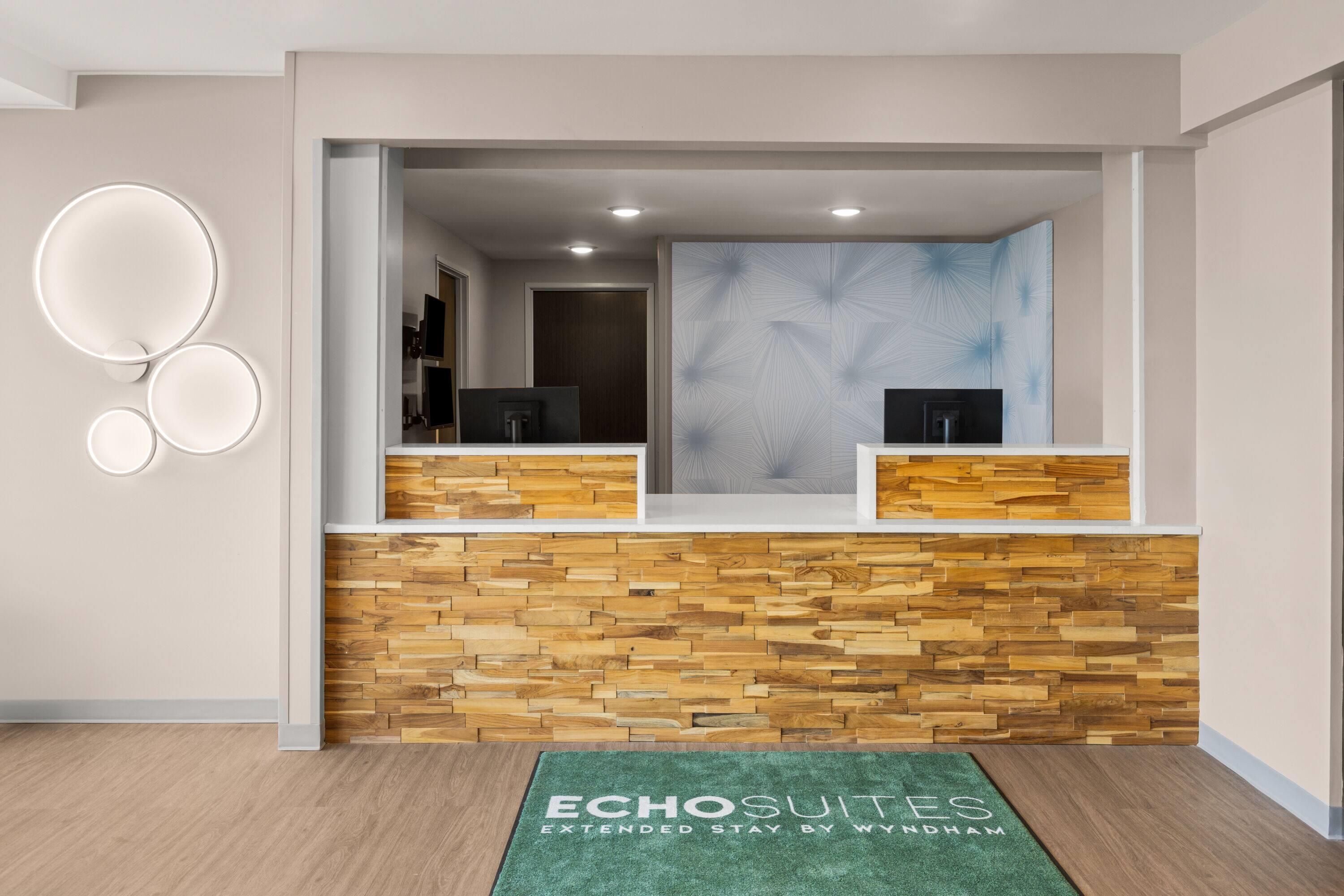 A reception area with a wooden wall, a reception desk, and a green mat with text.
