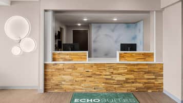 A reception area with a wooden wall, a reception desk, and a green mat with text.