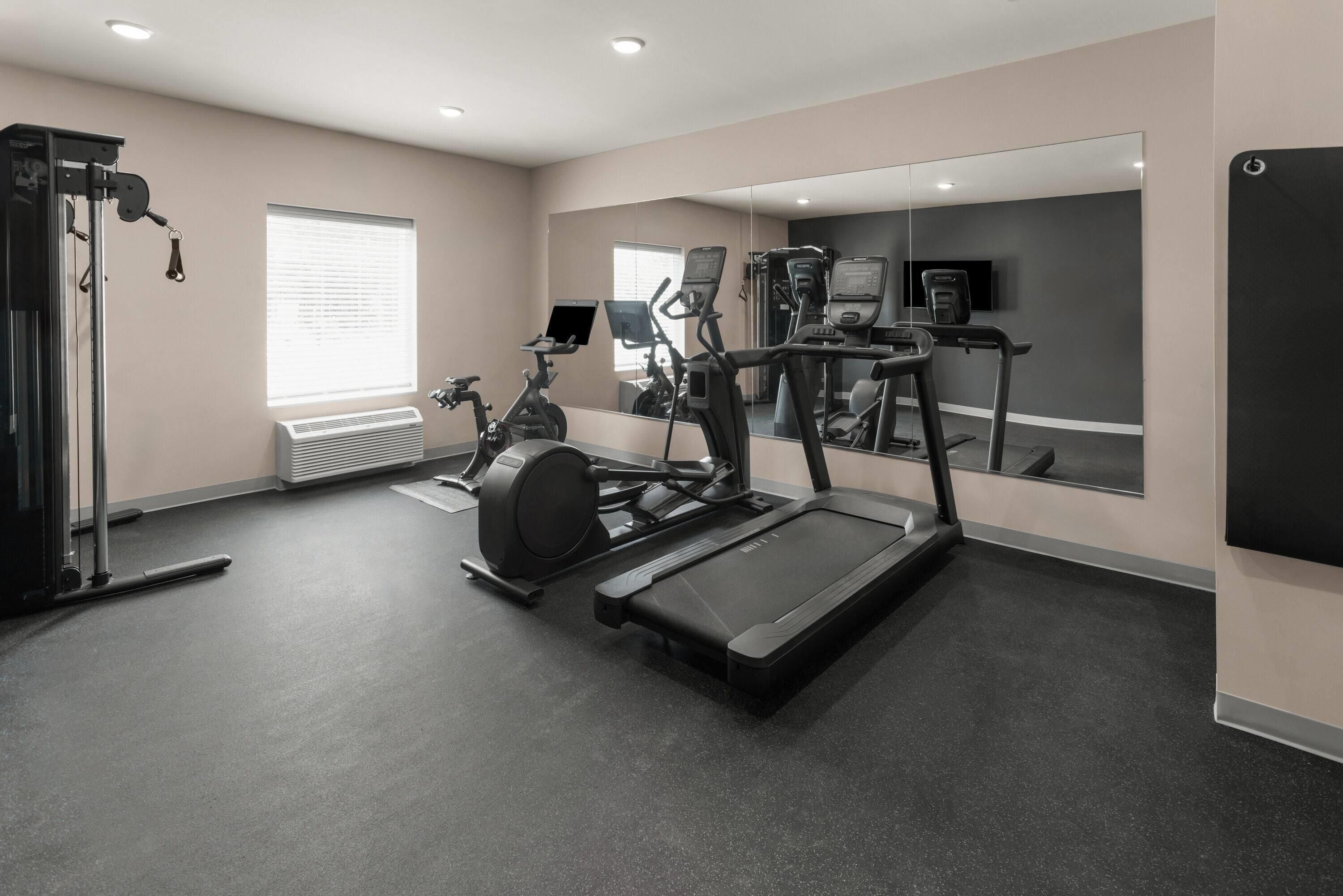 Un gimnasio con equipo de ejercicio, un espejo grande y una ventana con persianas.