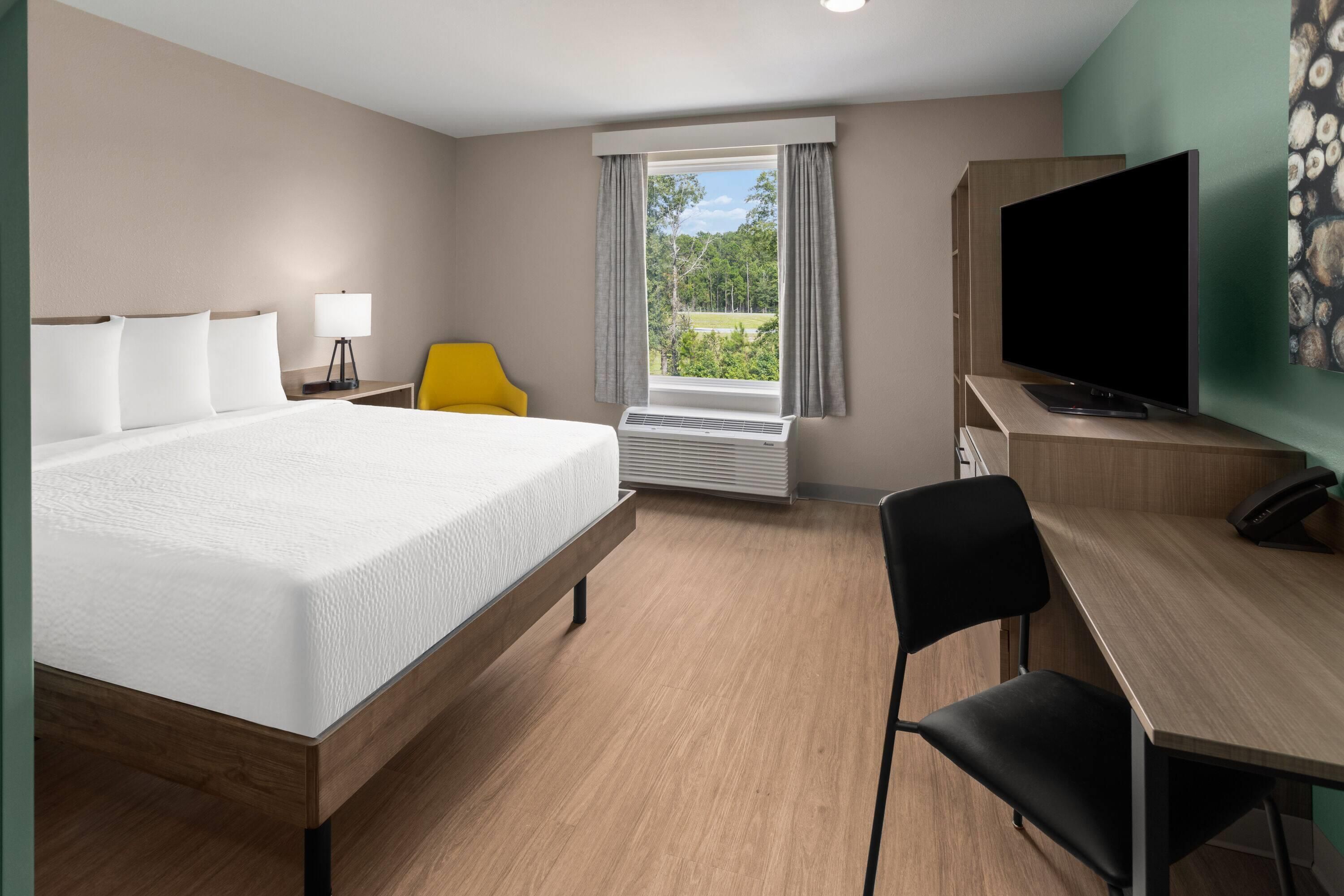 A hotel room with a bed, a desk, a chair, a television, and a window with a view of greenery.