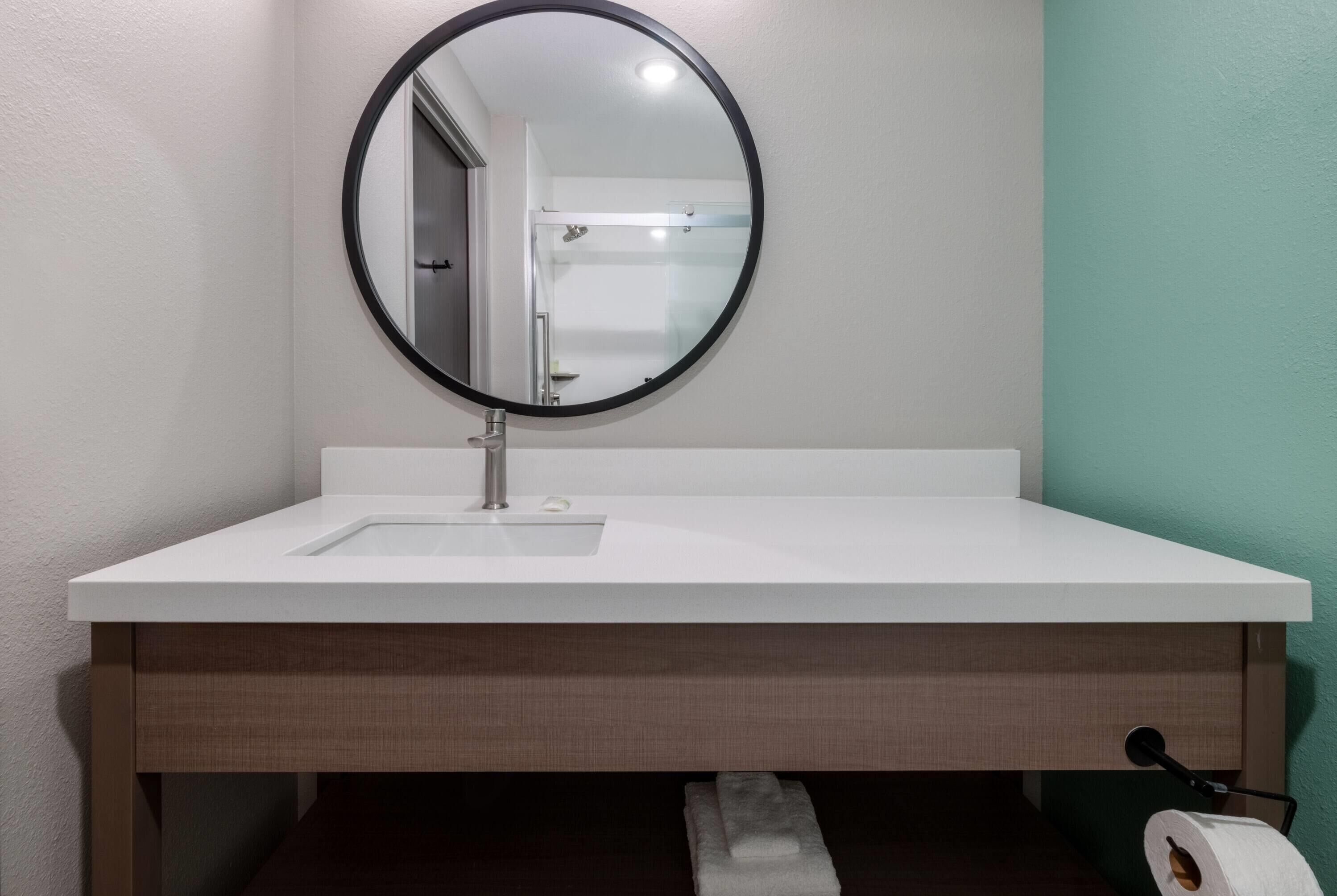 A bathroom with a white sink, a round mirror, and a towel dispenser.