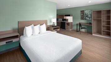 A hotel room with a large bed, a desk, a kitchenette, and a wardrobe.