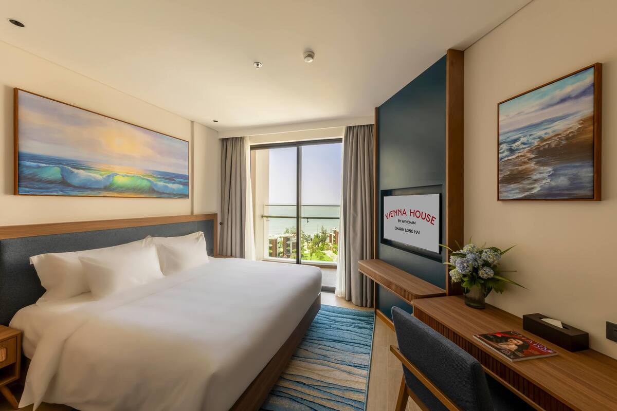 A hotel room with a bed, a desk, a TV, and a large window with curtains.