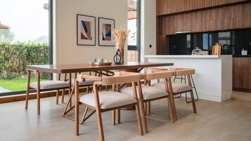 A modern kitchen with wooden cabinets, a dining area with a wooden table and chairs, and a view of the outdoors.