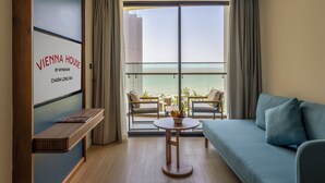 A modern hotel room with a large balcony, a sofa, a small table, and a wall-mounted TV.