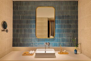 A bathroom with a rectangular mirror, a sink, a towel rack, and a potted plant.