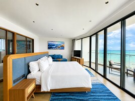 A modern hotel room with a large bed, a television, and a balcony with a view of the ocean.