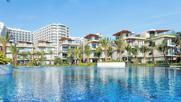 A resort with a swimming pool, multiple-story buildings, and palm trees.