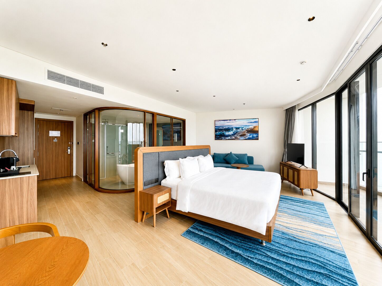A modern hotel room with a large bed, a seating area, a bathroom, and a view through large windows.
