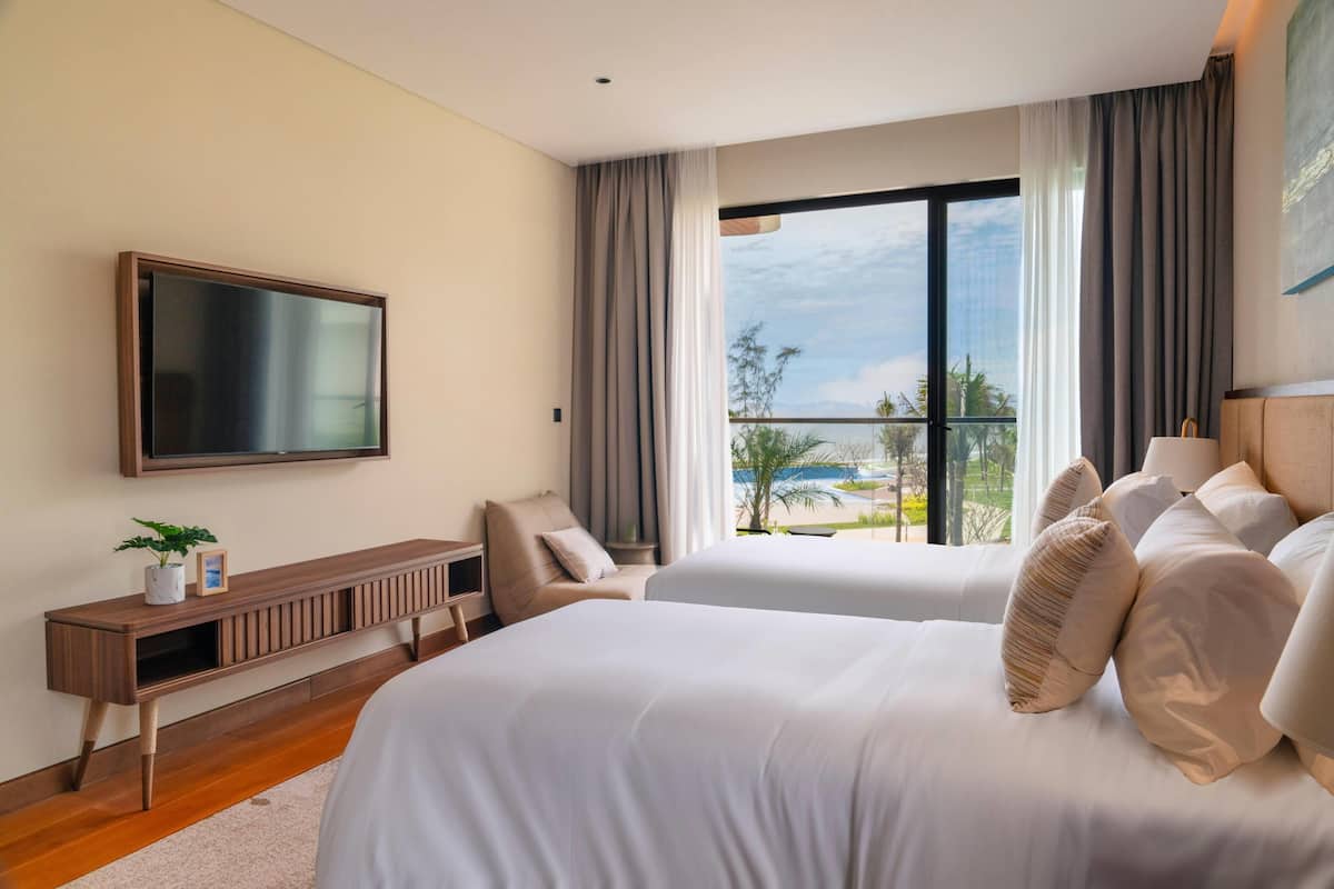A hotel room with two beds, a TV, a wooden console table, and a large window with a view.