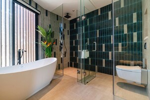 Egy modern fürőszoba, melyben egy különálló, lábazatos fürdőkád, egy üvegfalas zuhanyzó és egy WC található.