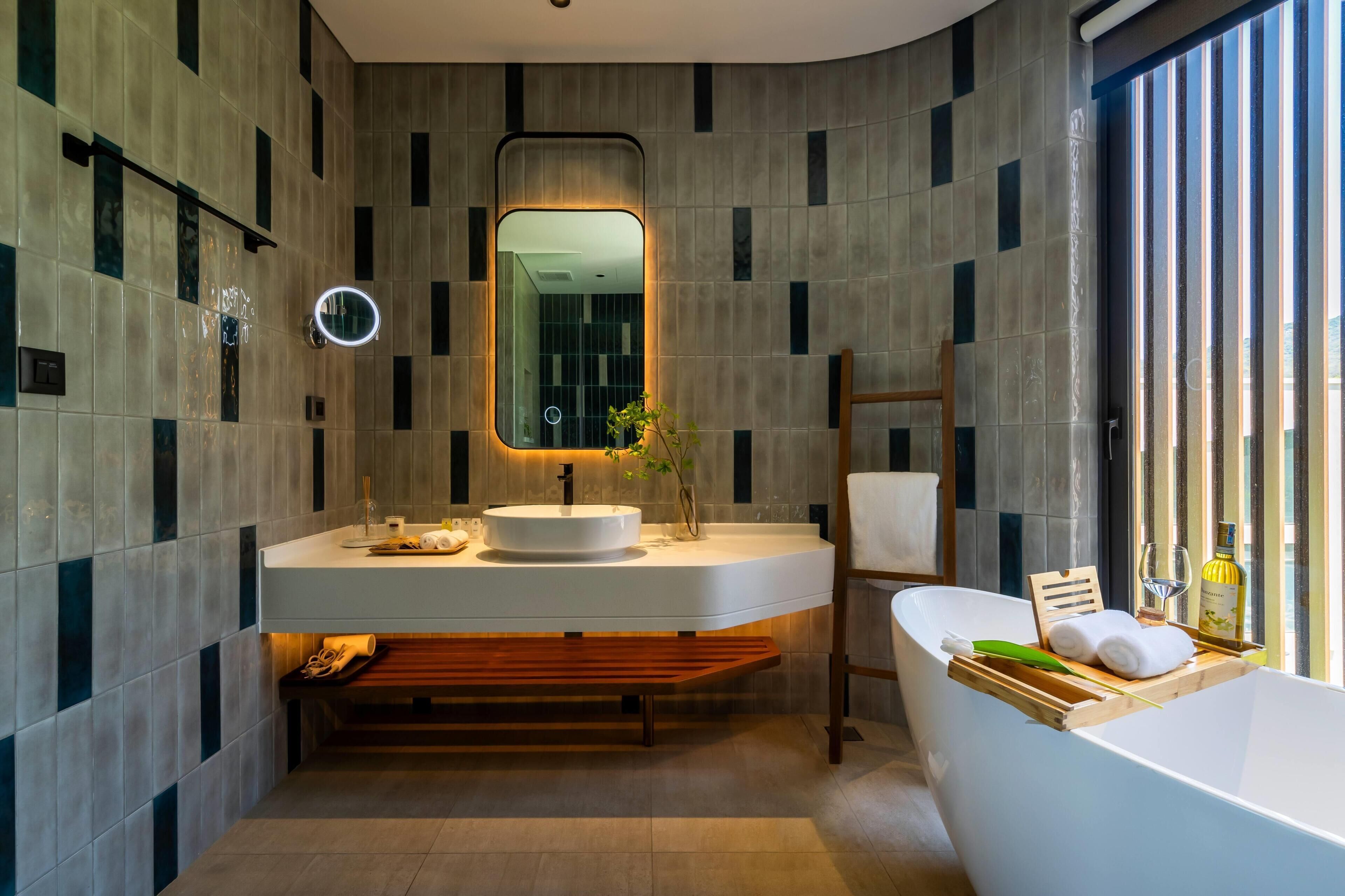 Un baño moderno con una bañera independiente, un espejo grande y un tocador con lavamanos y toallero.