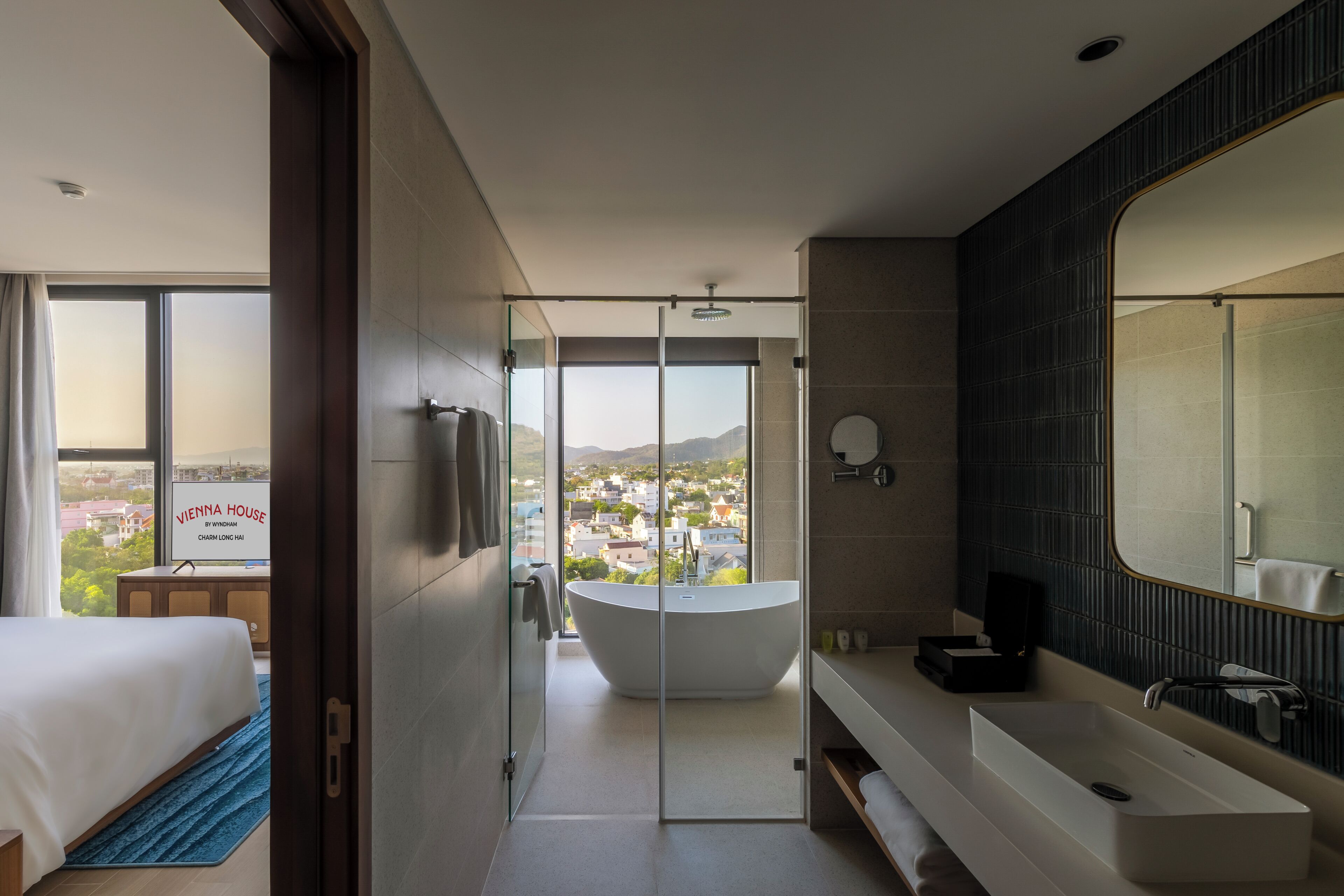 Une salle de bain d’hôtel moderne dotée d’une grande baignoire, d’une douche séparée, d’un grand miroir et offrant une vue sur le paysage urbain.