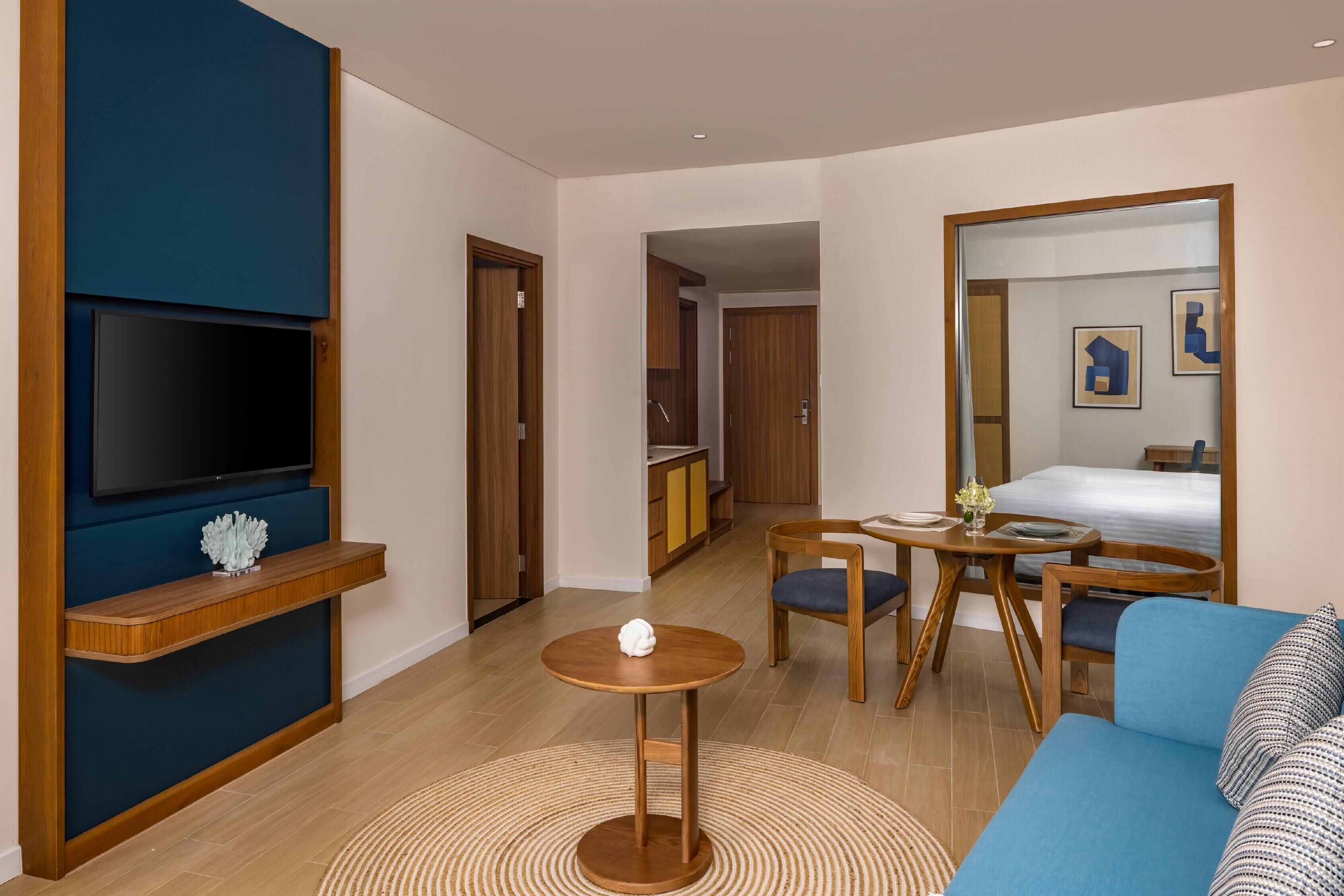 Una camera d'albergo moderna con TV, mobili in legno, un tavolino rotondo e uno specchio grande.