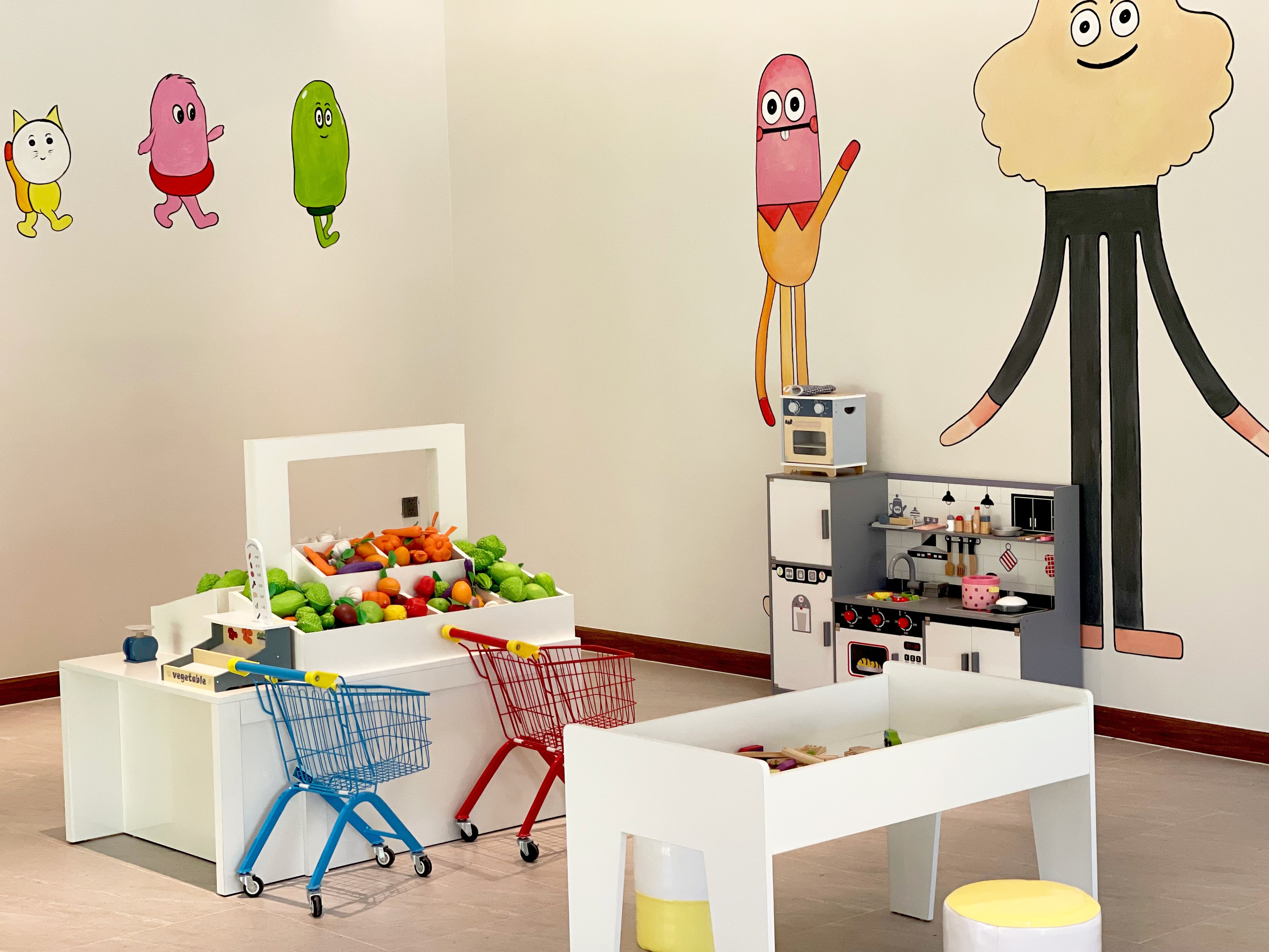 A children's play area with a vegetable display, shopping carts, and a kitchen playset.