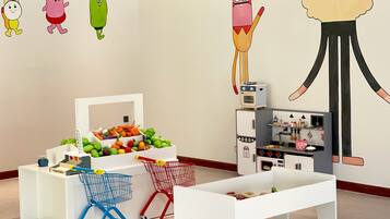 A children's play area with a vegetable display, shopping carts, and a kitchen playset.