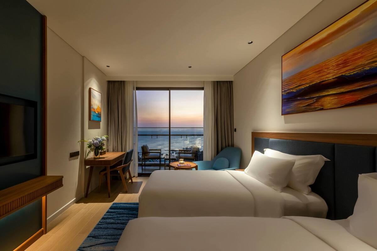 A hotel room with a bed, a desk, a chair, a TV, and a large window with a view.
