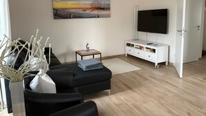 Un soggiorno con un divano nero, una televisione, un quadro e un mobile bianco.