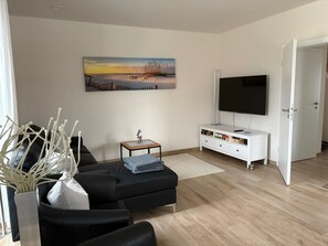 Ein Wohnzimmer mit einer schwarzen Couch, einem Fernseher, einem Gemälde und einer weißen Kommode.
