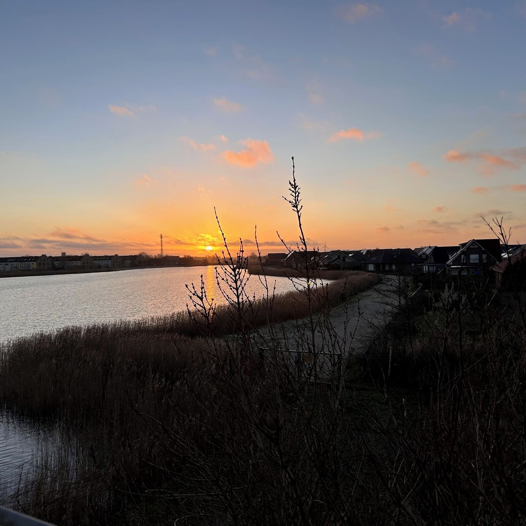 A sunset over a body of water with houses in the background.