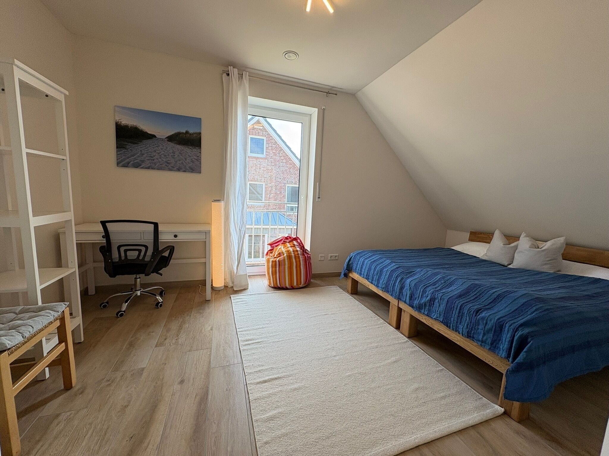 Una camera da letto con un letto, una scrivania, una sedia, una finestra e vista su un edificio.