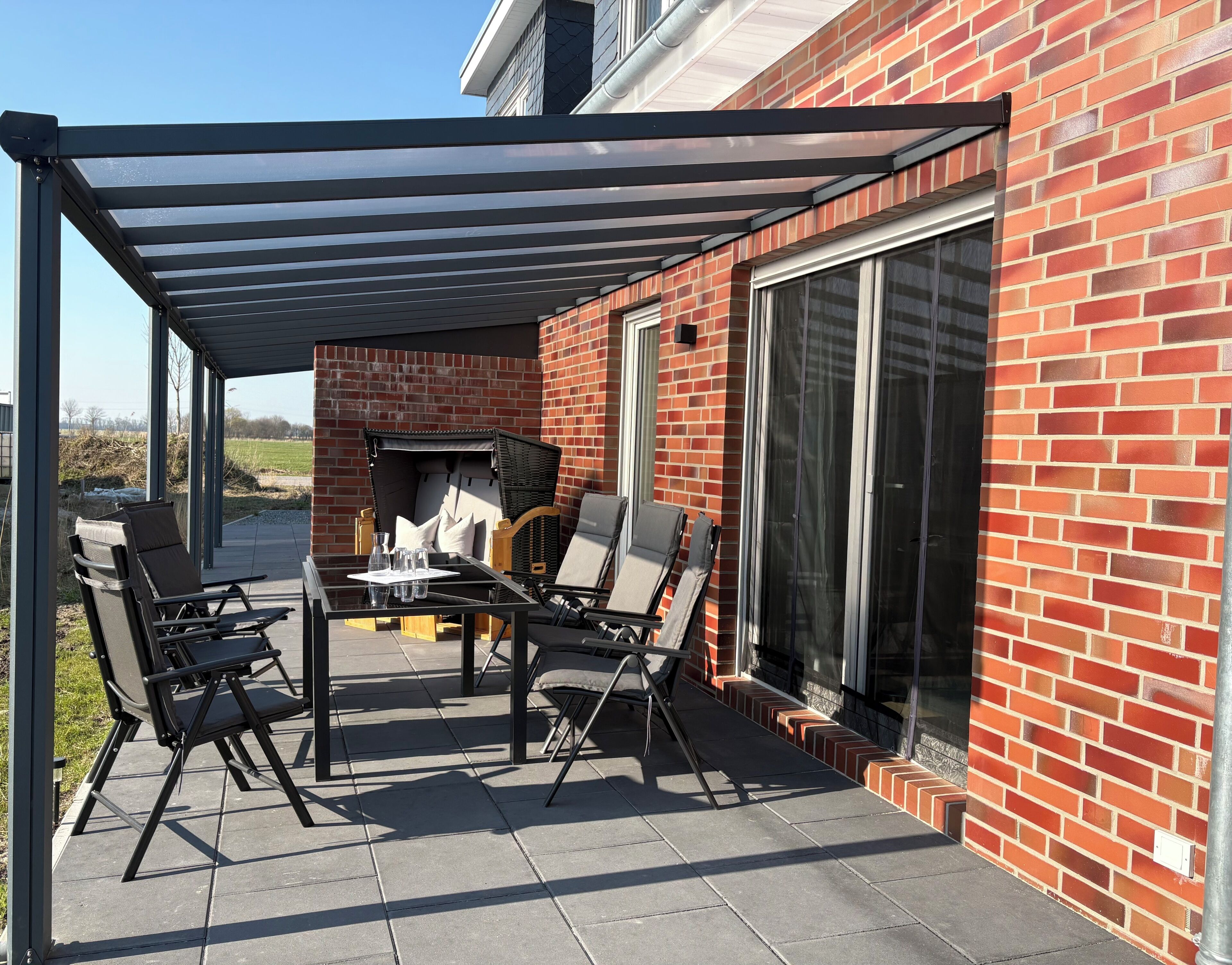 Eine Terrasse mit überdachter Sitzgruppe, einem Tisch und einem Grill.