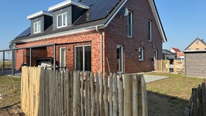 Una casa a due piani in mattoni con tetto spiovente, un portico coperto e una recinzione in legno.