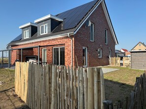 Ein zweistöckiges Ziegelhaus mit geneigtem Dach, einer überdachten Terrasse und einem Holzzaun.
