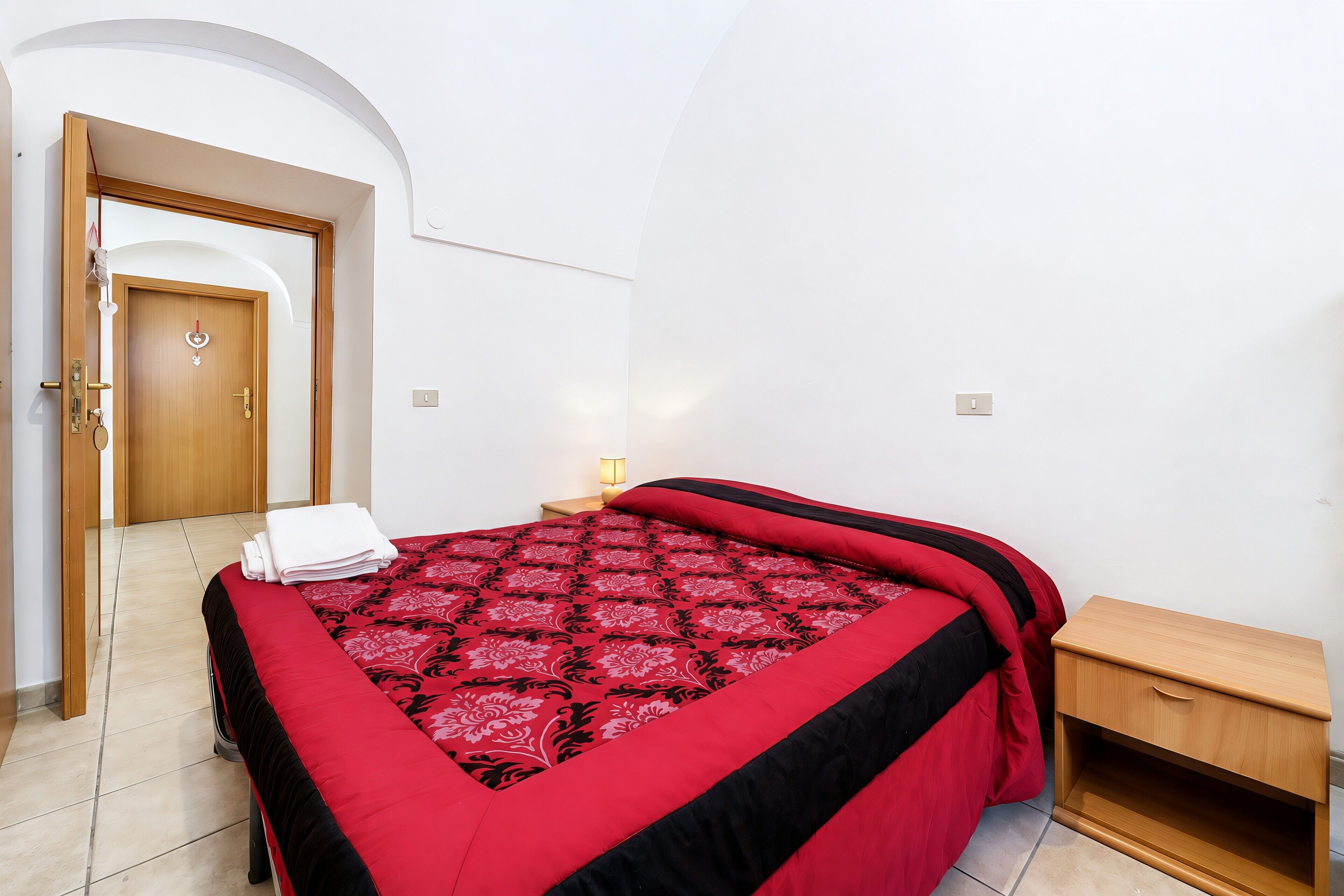 Une chambre à coucher avec un lit, une table de chevet en bois, une porte et un luminaire fixé au mur.