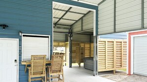 A covered outdoor area with a table and chairs, a garage door, and a wooden fence. - Cover RV Pad w/Large 45ft Destination RV & Outdoor Bar / Hot Tub (Bolivar Peninsula)
