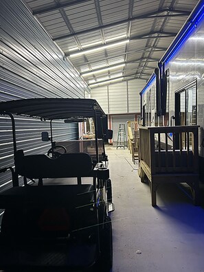 A warehouse interior with a forklift and a covered vehicle. - Cover RV Pad w/Large 45ft Destination RV & Outdoor Bar / Hot Tub (Bolivar Peninsula)