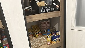 A kitchen pantry with shelves stocked with coffee supplies, snacks, and a coffee maker. - Cover RV Pad w/Large 45ft Destination RV & Outdoor Bar / Hot Tub (Bolivar Peninsula)