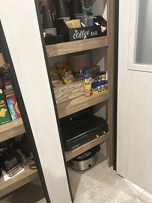 A kitchen pantry with shelves stocked with coffee supplies, snacks, and a coffee maker. - Cover RV Pad w/Large 45ft Destination RV & Outdoor Bar / Hot Tub (Bolivar Peninsula)