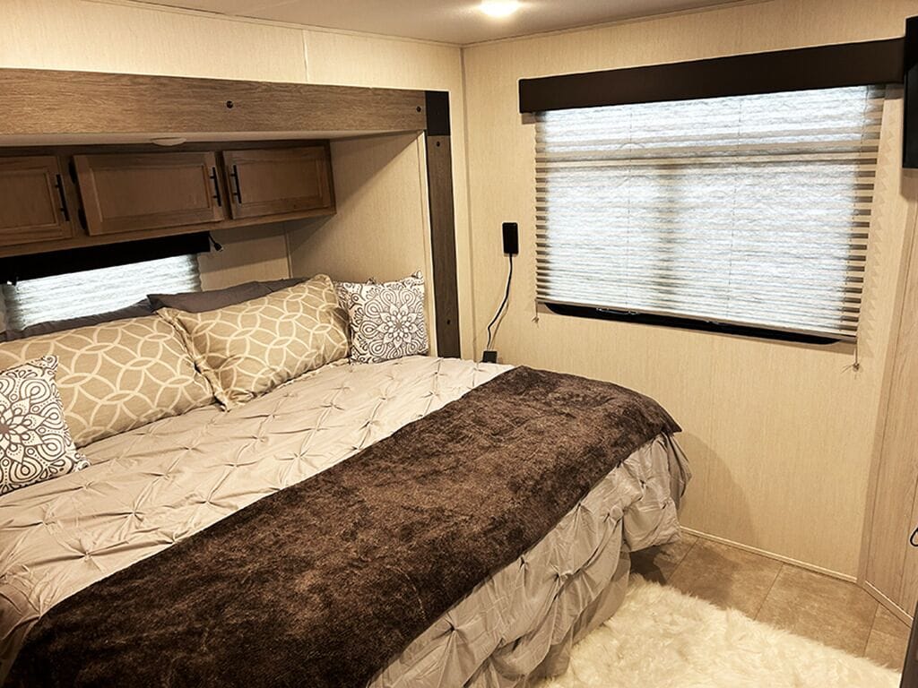 A bedroom with a bed, a window with blinds, and wooden cabinets.