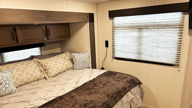 A bedroom with a bed, a window with blinds, and wooden cabinets. - Cover RV Pad w/Large 45ft Destination RV & Outdoor Bar / Hot Tub (Bolivar Peninsula)