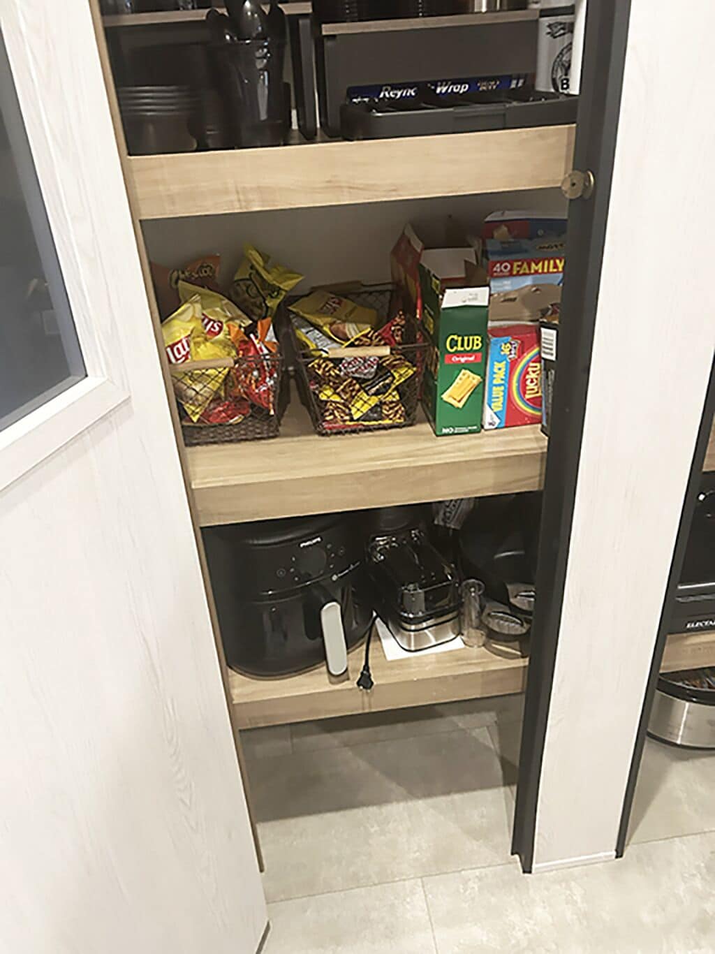 A kitchen pantry with shelves containing snacks, a coffee maker, and a box of Club Orange juice.