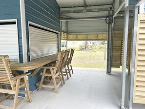 A covered outdoor area with a wooden table and chairs, metal railings, and a view of the surrounding area. - Cover RV Pad w/Large 45ft Destination RV & Outdoor Bar / Hot Tub (Bolivar Peninsula)