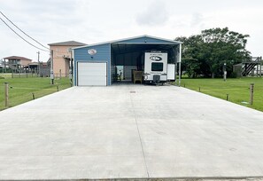A building with a covered entrance, a truck parked inside, and a clear sky. - Cover RV Pad w/Large 45ft Destination RV & Outdoor Bar / Hot Tub (Bolivar Peninsula)
